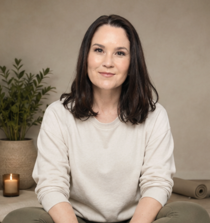 Jade Asher seated in a calm studio space with a plant and candle behind her
