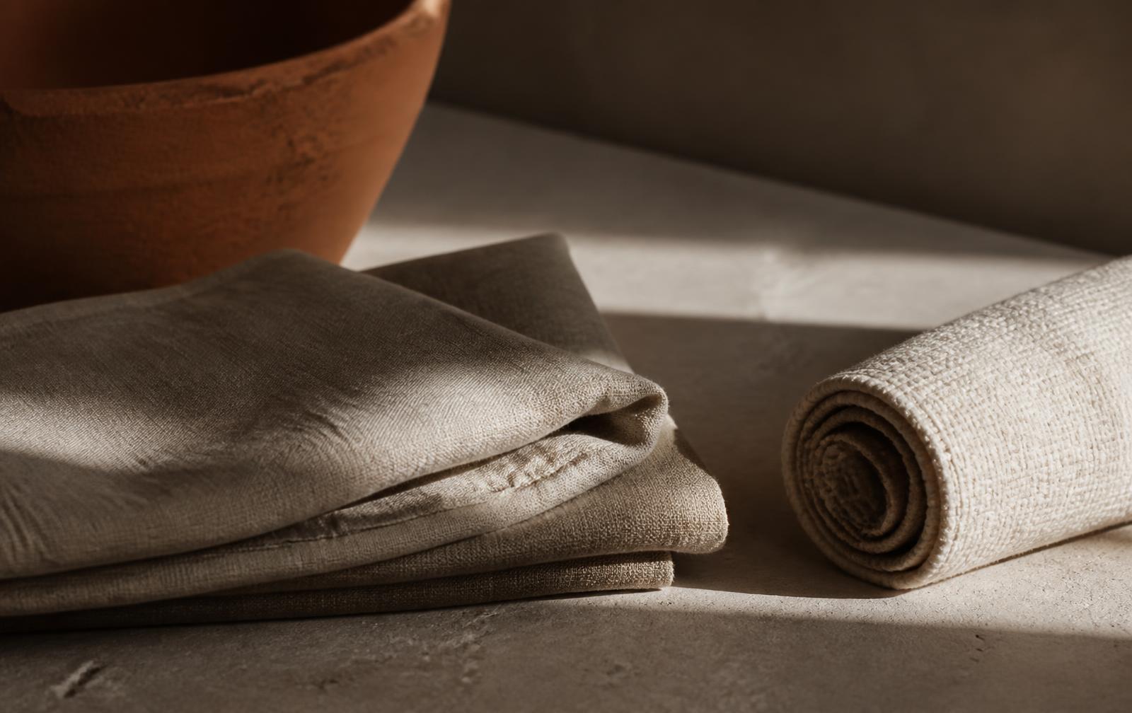 Folded linen and a rolled mat on a stone floor in warm afternoon light